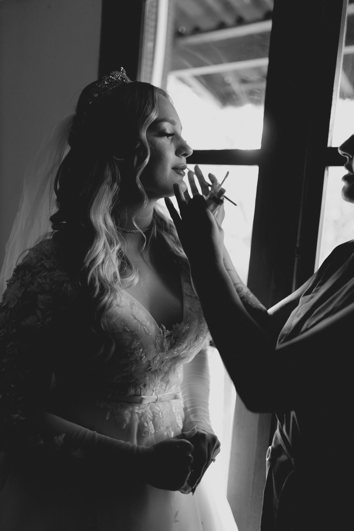 Bride in an elegant gown having her makeup finished in soft window light
