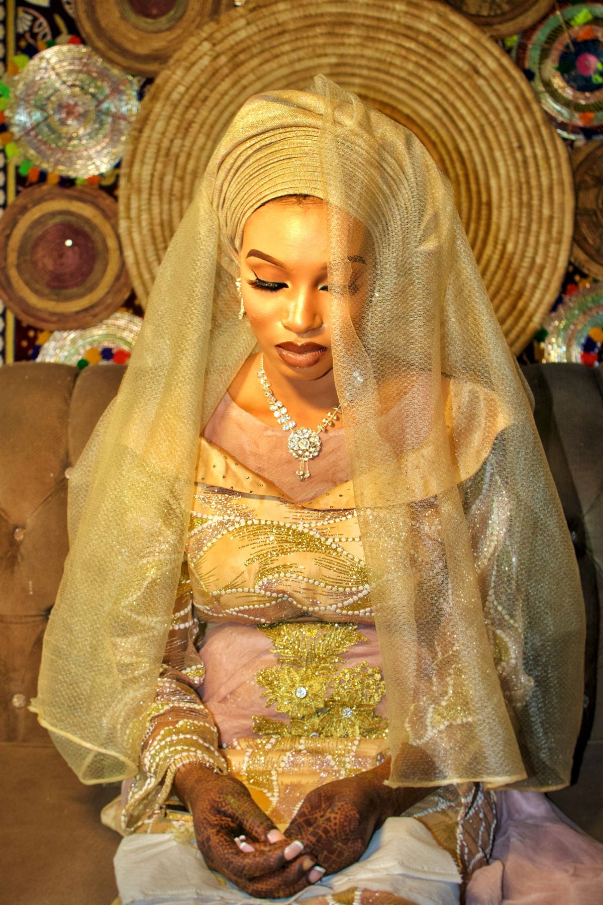 West African bride in a coral gele headwrap with bold luxurious bridal makeup